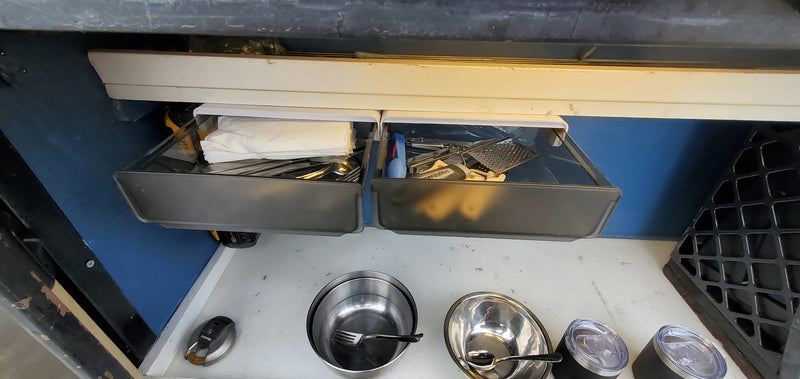 Compact RV rental kitchen storage: pull-out drawers with utensils, bowls, & tumblers on countertop. — photo 19