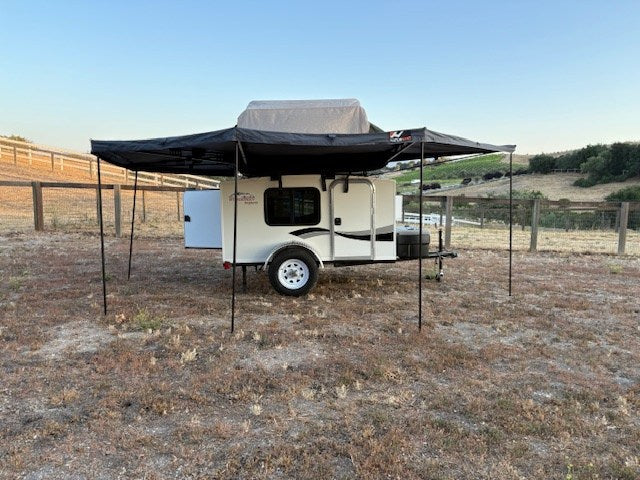 RV rental: Small camper trailer with a large awning and rooftop tent, parked in a scenic outdoor setting.