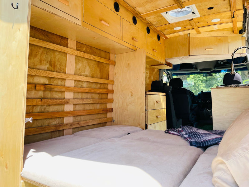 RV rental interior: custom wood camper van with comfortable bed, overhead storage, and built-in drawers for travel. — photo 3