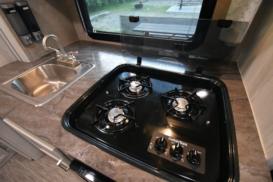 Compact RV kitchen with sink, 3-burner stove, and counter space, ideal for an rv rental.