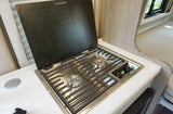 Inside an RV rental: a compact stainless steel 2-burner gas cooktop with an open cover built into a white countertop.