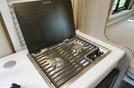Inside an RV rental: a compact stainless steel 2-burner gas cooktop with an open cover built into a white countertop.