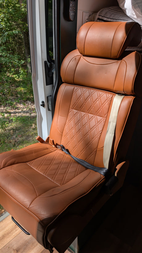 Stylish brown leather seat in an RV rental, featuring quilted details. Enjoy comfortable travel with nature views from the open door.