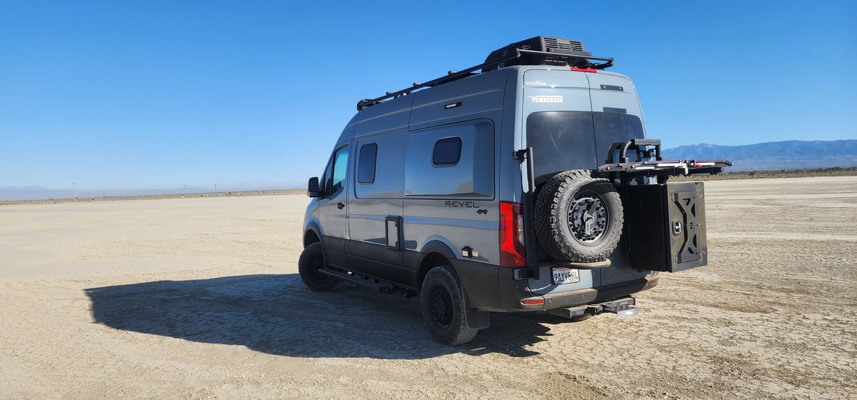 A gray Revel 4x4 camper van, perfect for an rv rental adventure, parked on a wide desert playa under a clear blue sky.
