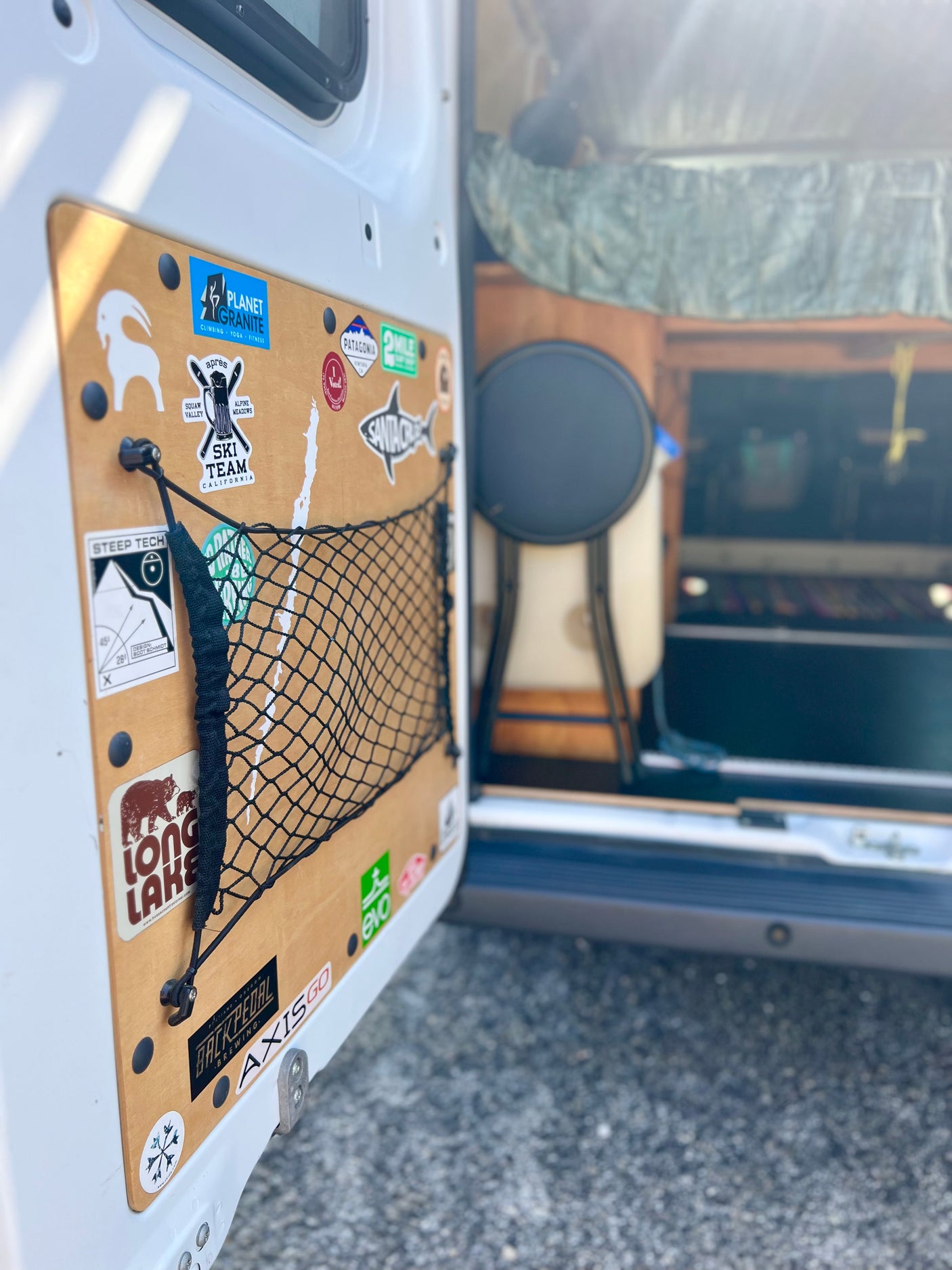 The customized door of an rv rental features a wooden panel with numerous outdoor adventure stickers and a practical storage net.