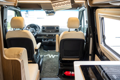 Interior of a modern RV rental: A clean cockpit features tan leather seats, a Mercedes-Benz dashboard, and a visible fire extinguisher.