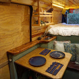 This inviting RV rental offers a compact kitchen, dining table set for two, & elevated bed within its cozy wood interior.