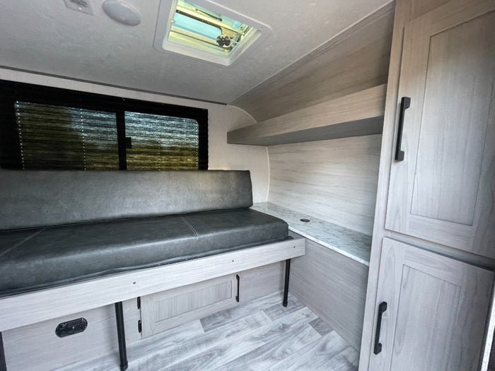 Inside a compact RV rental: gray bench seating, light wood-look interior, storage cabinets, and skylight.