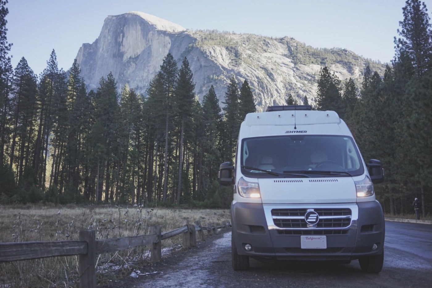  beside a glowing fire.|A white pop-top RV rental camper van parked on pavement in a dense forest campsite. A picnic table is nearby.|RV rental with bikes on back — photo 5
