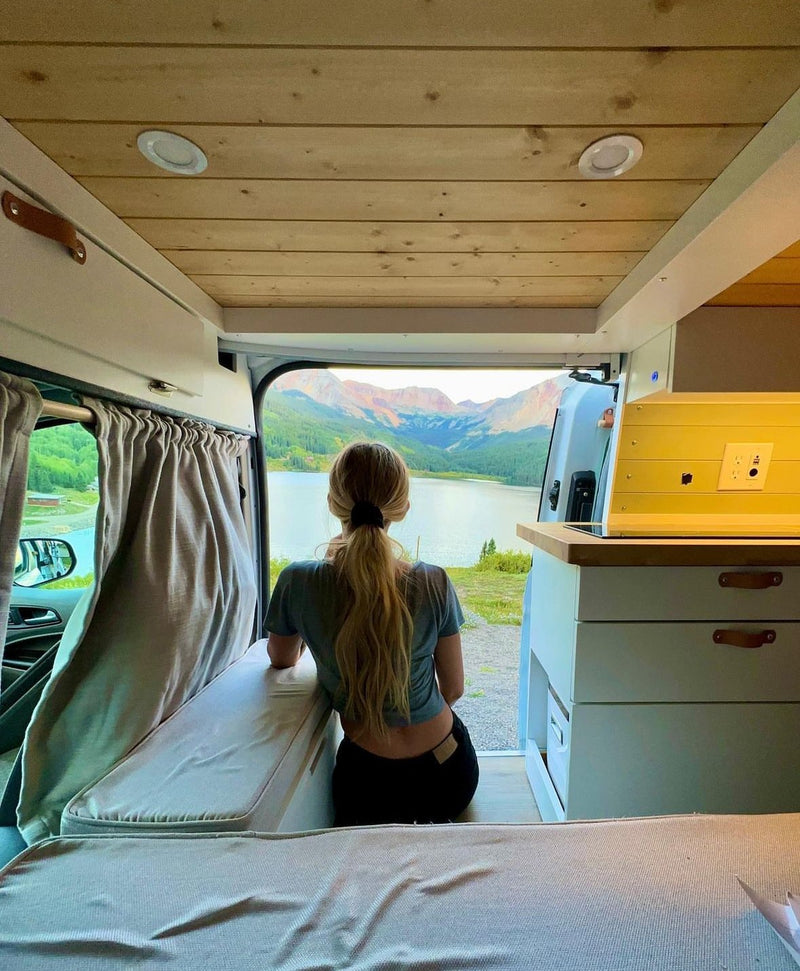 RV rental interior: Woman overlooks stunning lake & mountain scenery from her cozy camper van. Van life.|Inside an RV rental: a modern converted van with a kitchen — photo 1