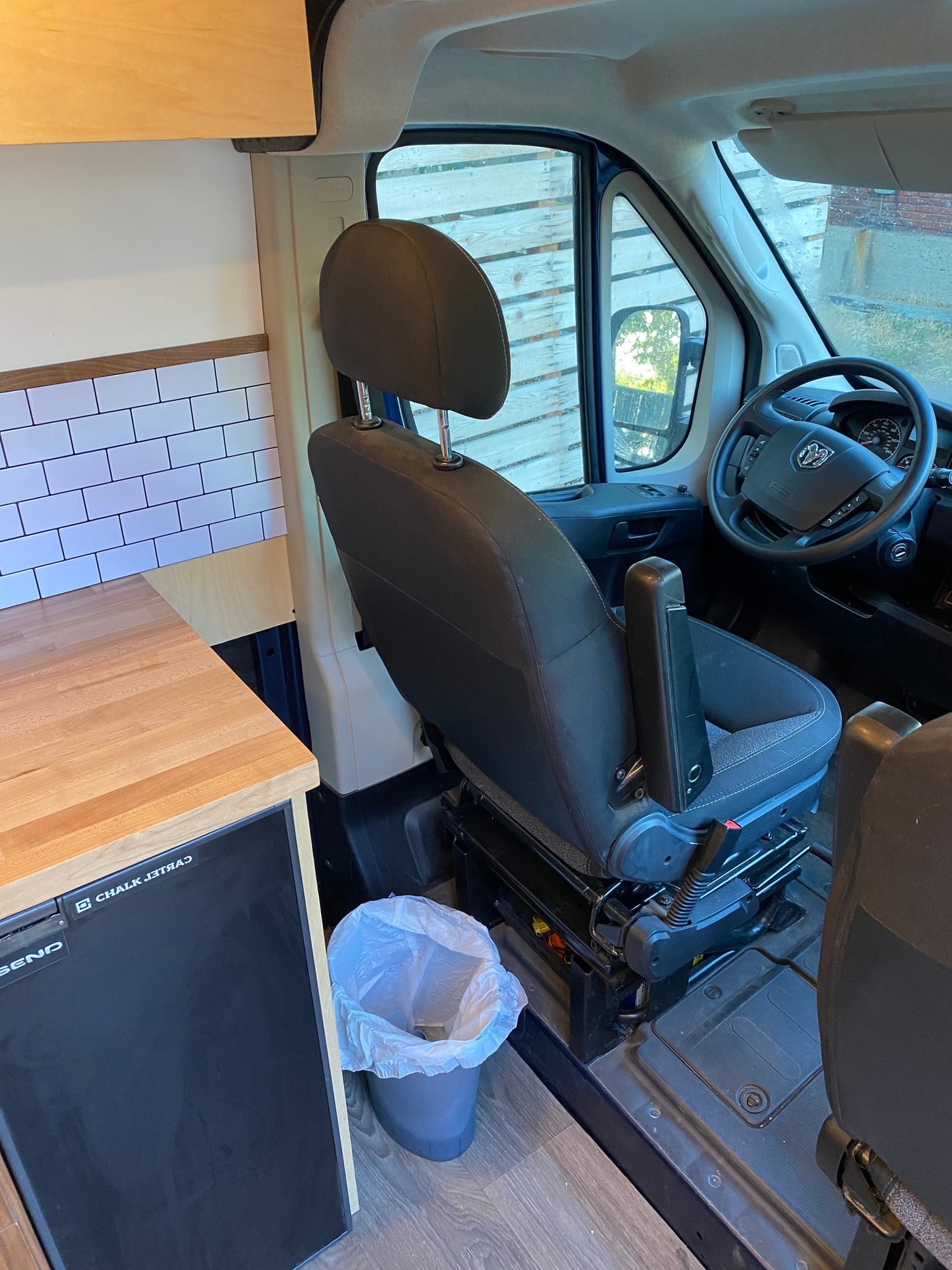 RV rental van interior. Driver's seat, Ram steering wheel, and a custom kitchen area with wood counter, subway tile backsplash, and mini-fridge. — photo 6