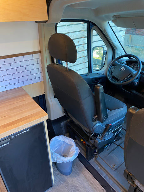 RV rental van interior. Driver's seat, Ram steering wheel, and a custom kitchen area with wood counter, subway tile backsplash, and mini-fridge.
