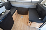 Compact rv rental interior: black dinette benches, light wood floor with table base, and compact kitchen/fridge. Ready for adventure.