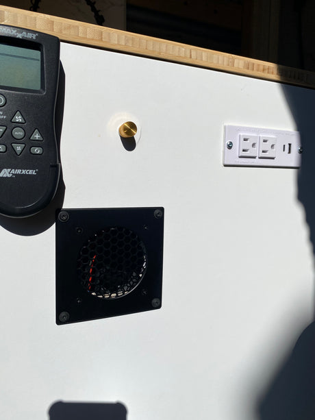 RV rental interior detail: Airxcel AC remote, multi-outlet with USB, and a ventilation fan on a clean white panel.