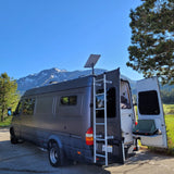 This RV rental camper van, parked amidst mountains, shows its open rear doors and equipped camping setup.
