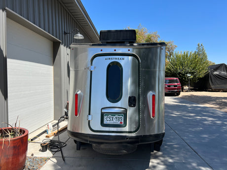 Silver Airstream travel trailer, rear view, parked by a garage. Ready for your next RV rental adventure!