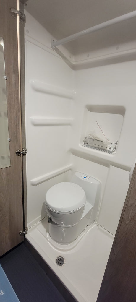 Inside a compact white wet bath of an rv rental, featuring a toilet, shower bar, and drain.