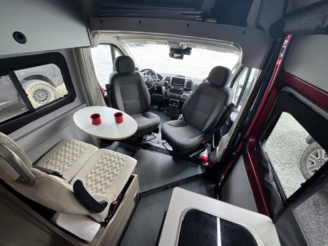 RV rental interior: Swiveling front seats face a dinette table with two red mugs, creating a versatile living space.