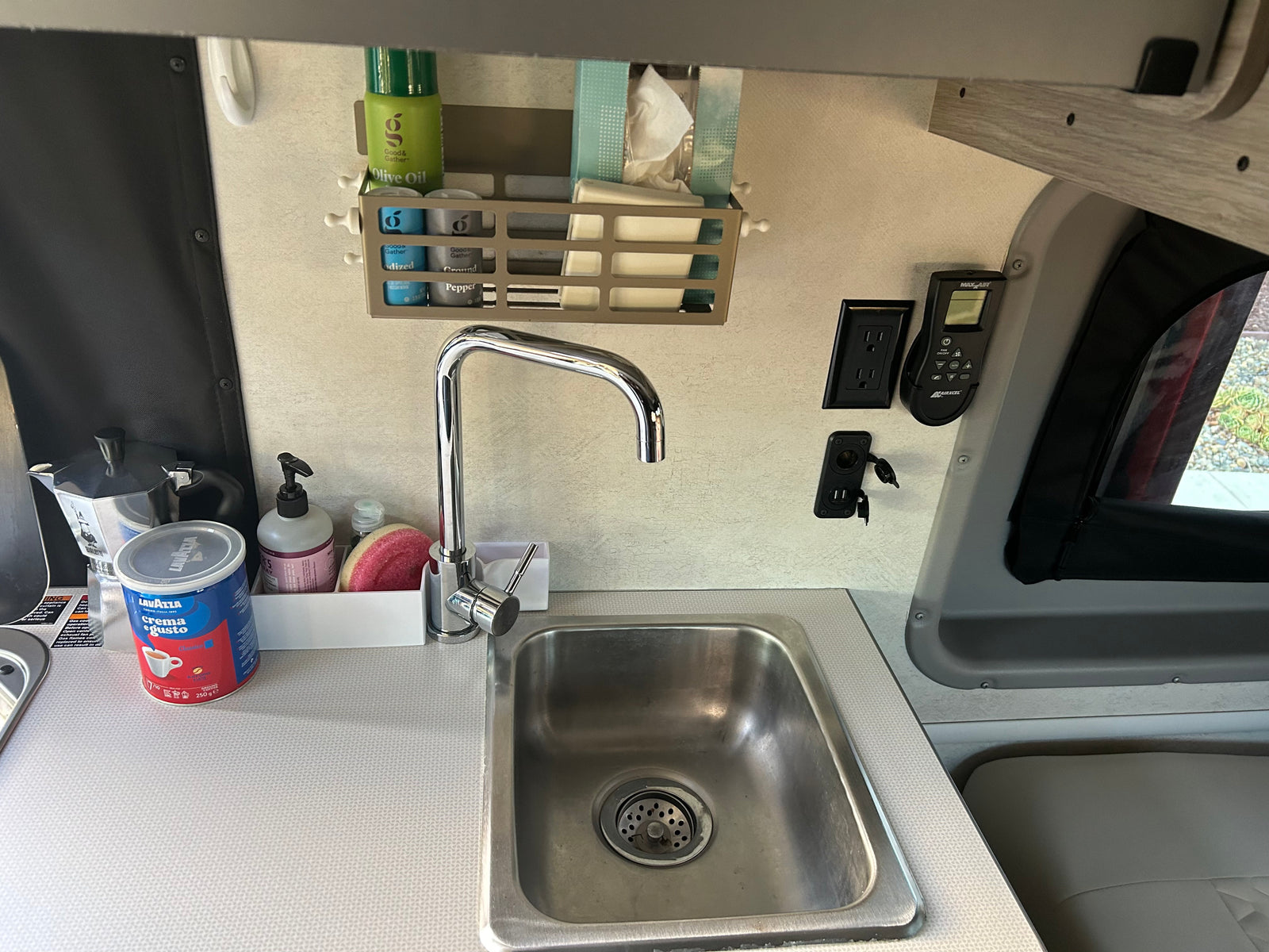 A compact rv rental kitchen featuring a stainless steel sink, coffee setup, and wall-mounted spice organizer, ready for adventures.