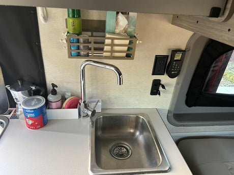 A compact rv rental kitchen featuring a stainless steel sink, coffee setup, and wall-mounted spice organizer, ready for adventures.