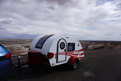 Teardrop RV rental hitched to a car, parked overlooking a vast desert landscape under cloudy skies.