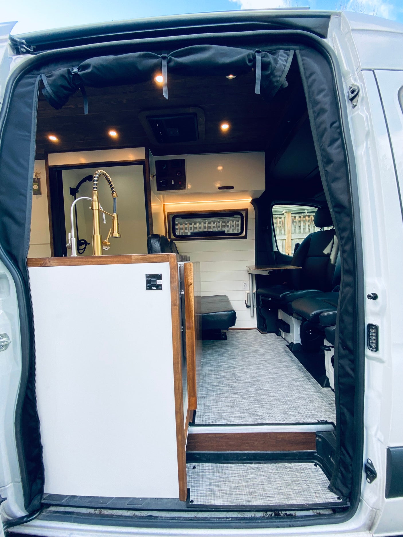 This RV rental's interior features a modern kitchen with a gold faucet, dark wood ceiling, and comfortable seating.