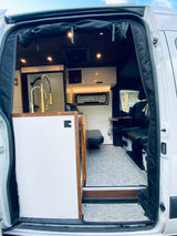 This RV rental's interior features a modern kitchen with a gold faucet, dark wood ceiling, and comfortable seating.