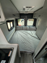 Comfortable RV rental interior with a large bed, plaid pillows, kitchen counter, and overhead storage, ideal for compact travel.
