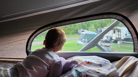 Cozy morning view from an RV rental. Child watching fellow campers through the screen window. Perfect for families!