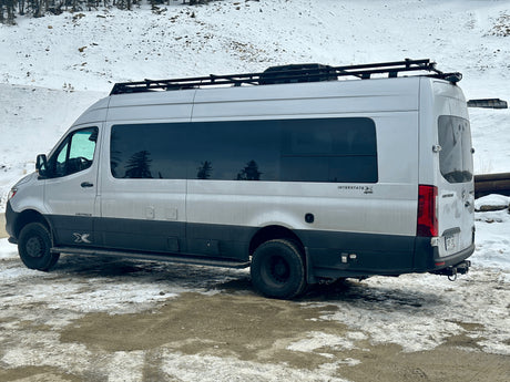 Silver Airstream Interstate X 4x4 RV rental van with roof rack, parked in a snowy landscape, ready for adventure.