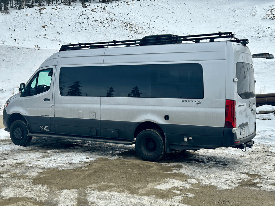 Silver Airstream Interstate X 4x4 RV rental van with roof rack, parked in a snowy landscape, ready for adventure.