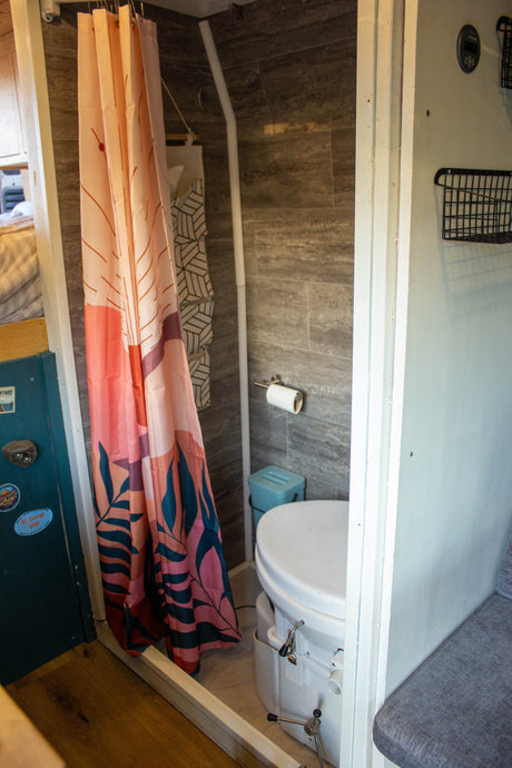 RV rental bathroom features a patterned shower curtain, composting toilet, and tiled walls in a compact design.