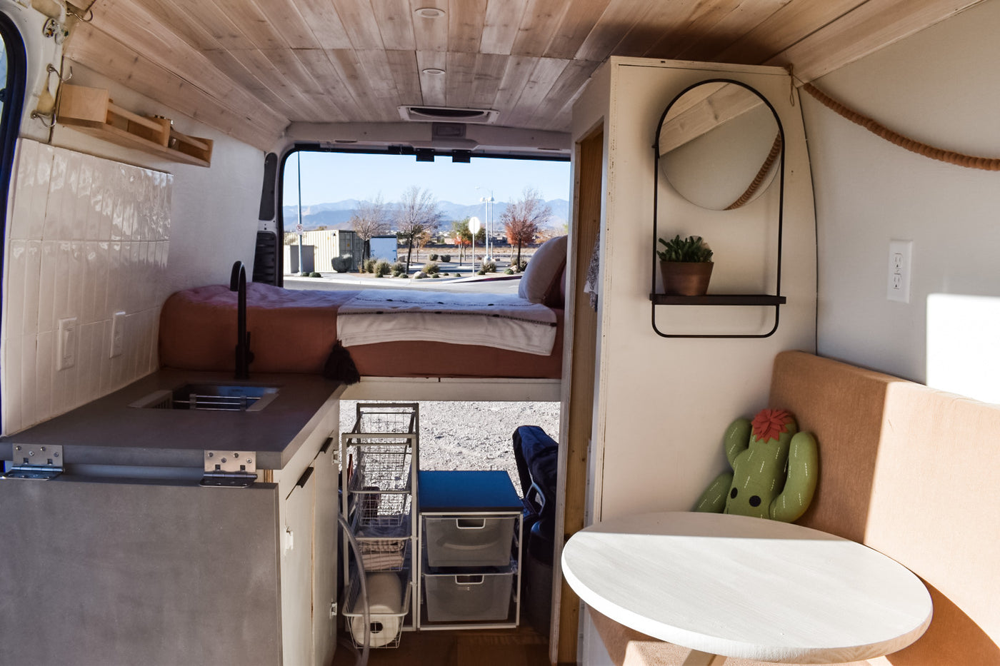 Custom RV rental interior: a bright camper van featuring a compact kitchen, elevated bed, and cozy dining area with outdoor views. — photo 12