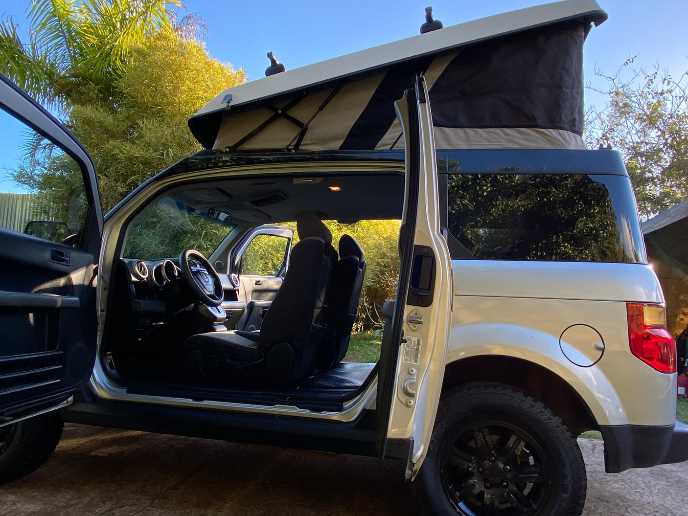 Light-colored Honda Element pop-top camper van with open doors, ready for your next rv rental adventure. Shows spacious interior.