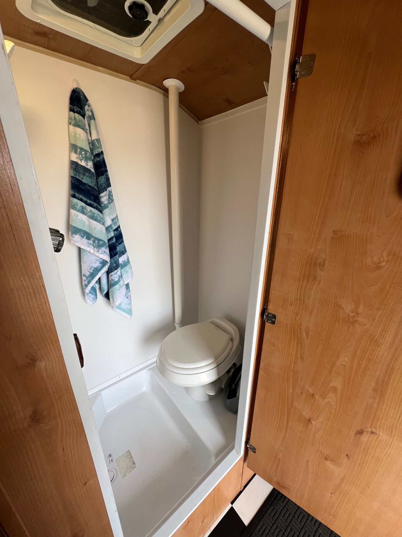 Compact RV rental bathroom featuring a toilet, shower pan, and overhead vent, with a towel hanging.