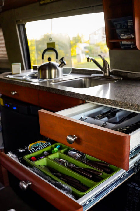 Compact RV rental kitchen features a sink, stovetop, and an organized pull-out drawer with cutlery for efficient living on the road.