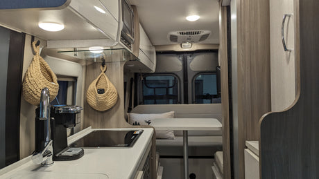 Explore a modern rv rental with a functional kitchen featuring a sink, stovetop, and coffee maker, plus a cozy dining area.