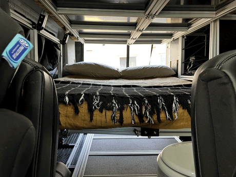 Inside an RV rental: a comfy sleeping area with a bed, overhead support structure, and integrated toilet, ready for adventure.