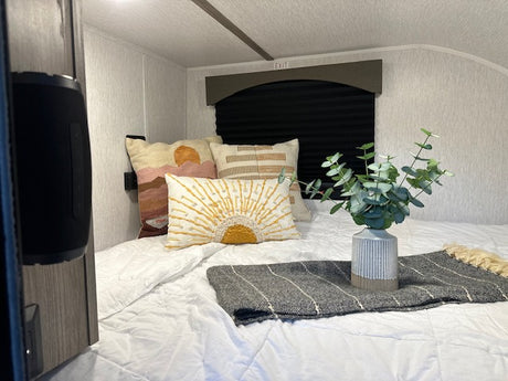 Experience comfort in this RV rental bedroom: bed with white linens, decorative pillows, speaker, and eucalyptus decor.