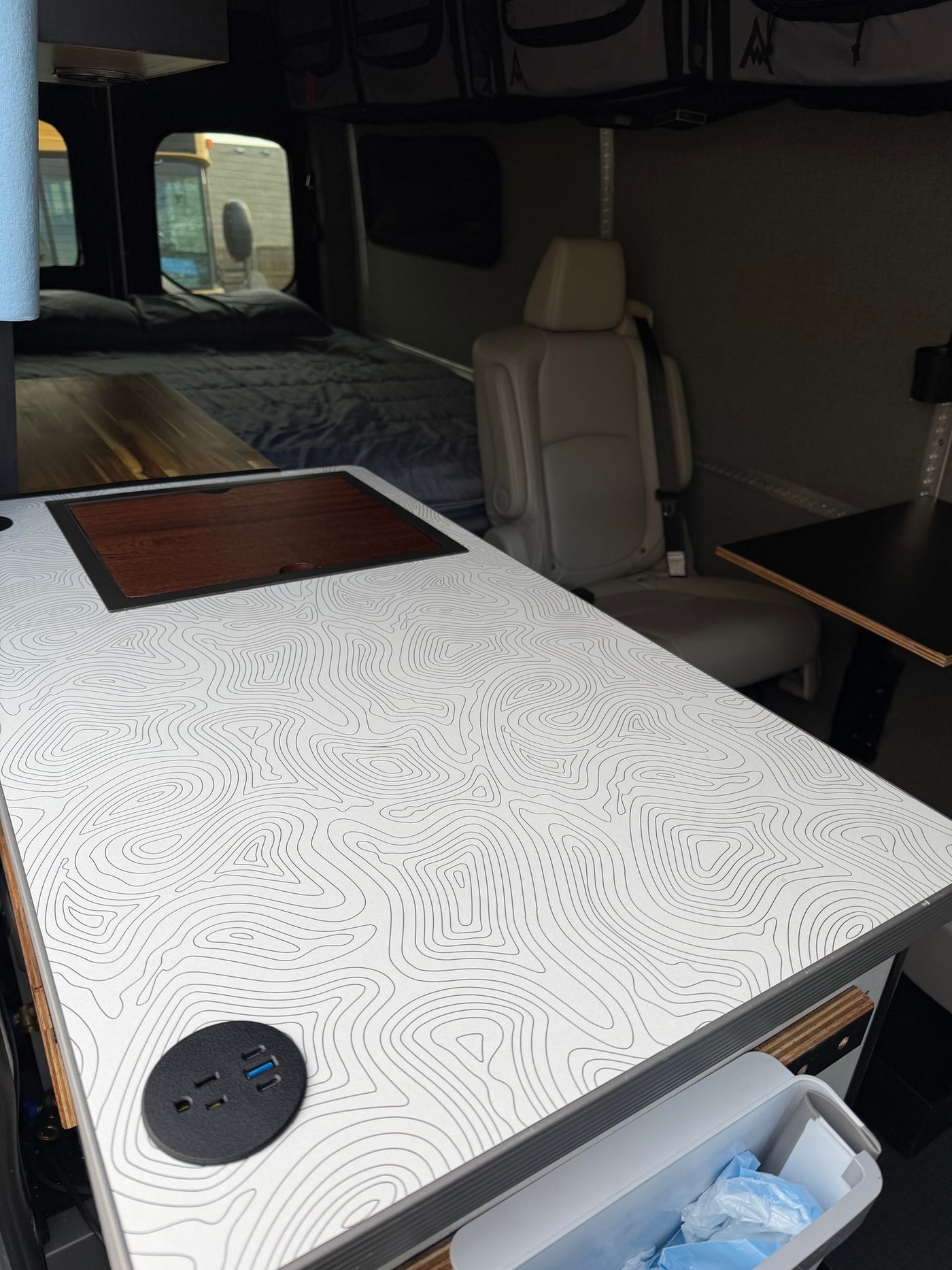Inside an RV rental camper van: a customizable table with contour map design, embedded power outlets, and a cozy bed for mobile living. — photo 15