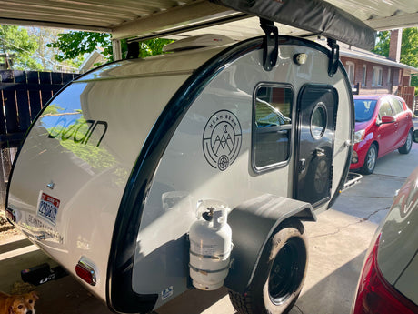 Stylish Bean teardrop camper with all-terrain tires and propane tank, ideal for your next RV rental or personal outdoor adventure.