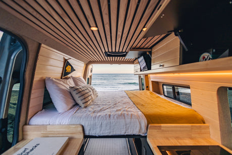 RV rental: Plush camper van interior with a cozy bed, opening to a stunning ocean view. Perfect for beach adventures.
