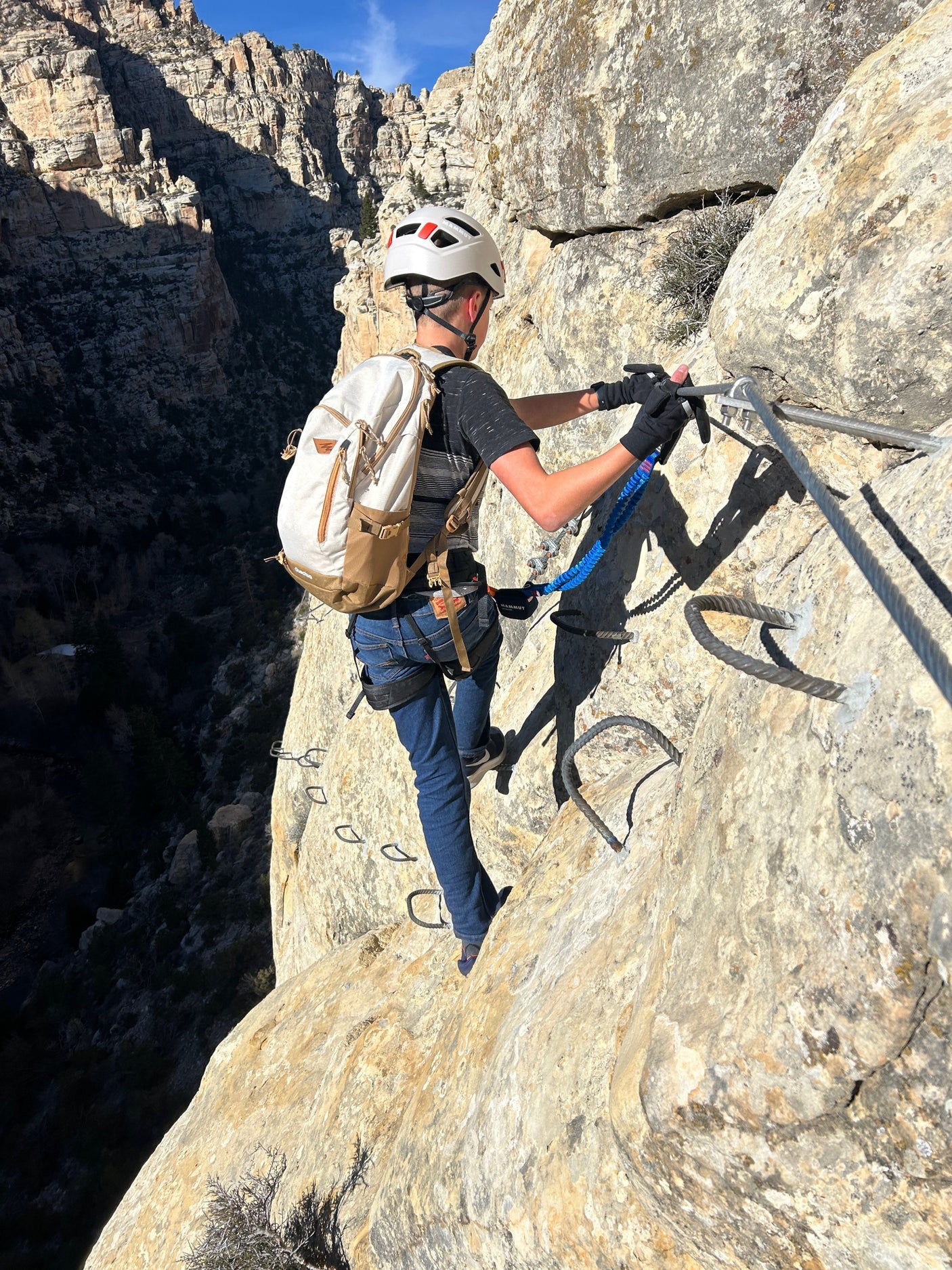 Person on a via ferrata route, securely attached to safety cables & rungs, with deep canyon views. Perfect for an RV rental adventure!