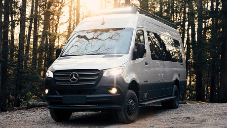 Explore nature with this Mercedes Sprinter camper van RV rental, parked on a dirt road in a sunlit forest. Off-road adventure.