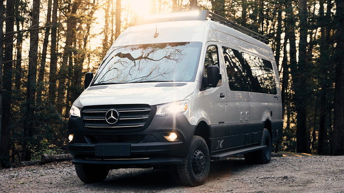 Explore nature with this Mercedes Sprinter camper van RV rental, parked on a dirt road in a sunlit forest. Off-road adventure.