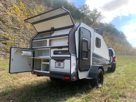 Compact RV rental travel trailer with its rear kitchen open, perfect for camping adventures.