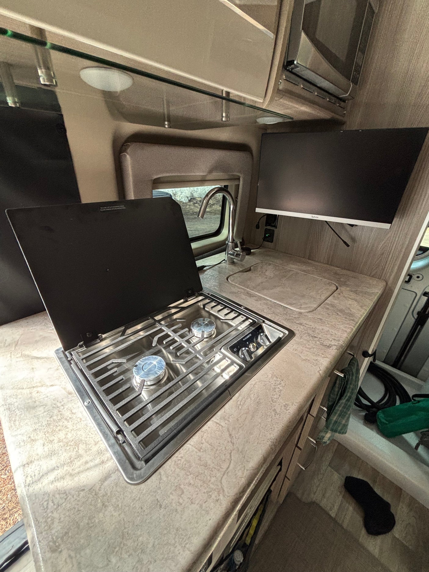 Well-equipped RV rental kitchen: two-burner stove, sink, ample counter space, and a mounted TV for your journey.