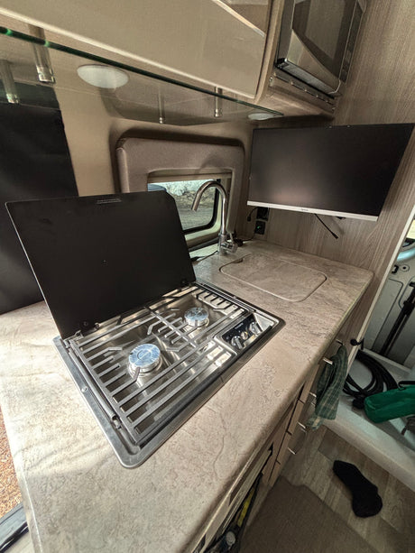 Well-equipped RV rental kitchen: two-burner stove, sink, ample counter space, and a mounted TV for your journey.