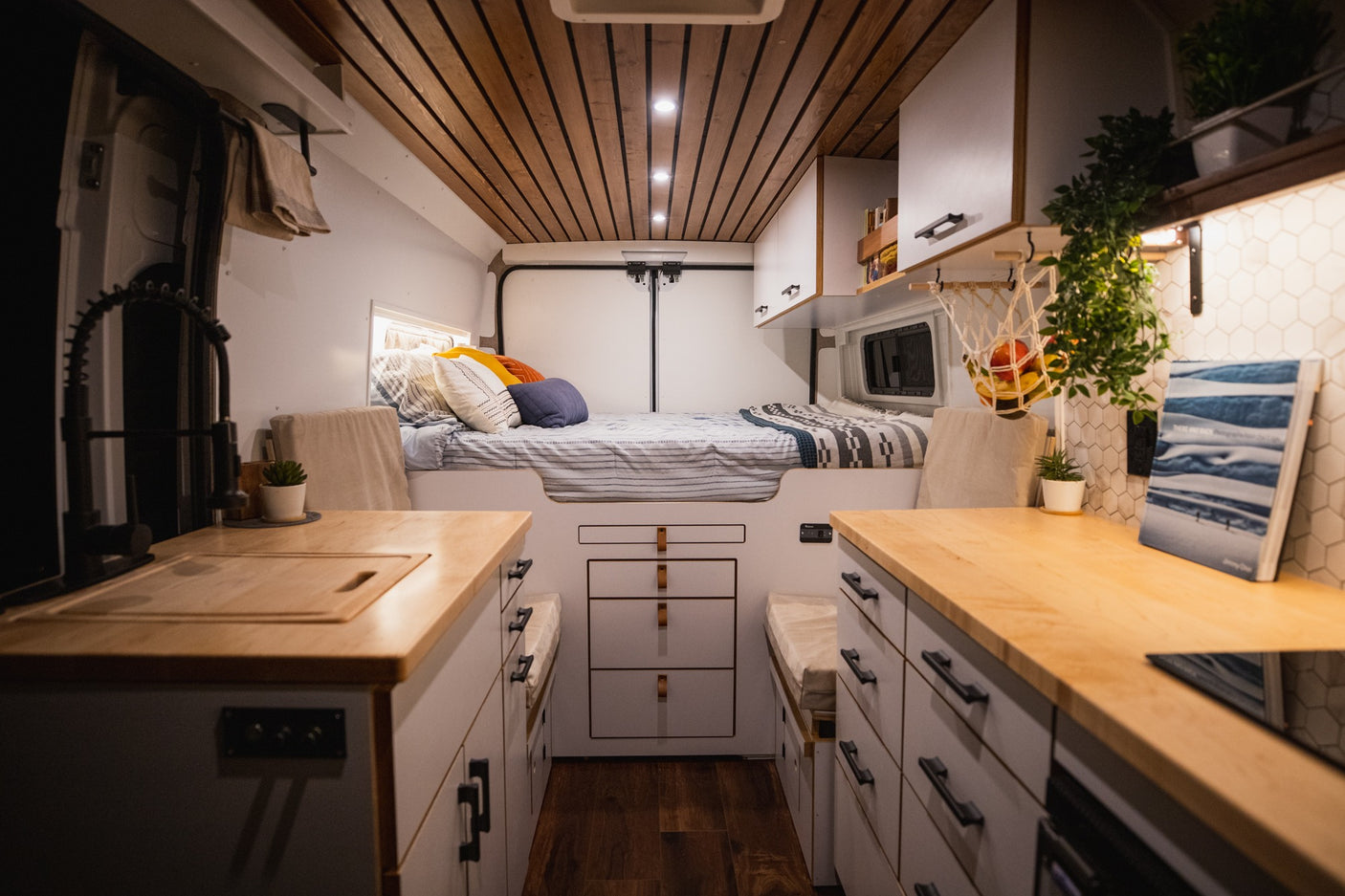 Discover this stylish RV rental! A well-appointed camper van interior features a raised bed, dual kitchen counters, and clever storage.