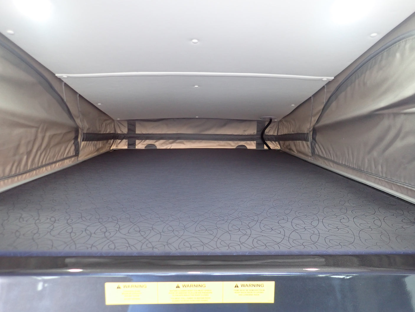 Inside an RV rental pop-top, showing the elevated sleeping area with a patterned mattress & fabric sides.